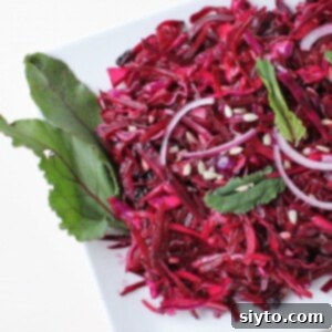 Shredded red cabbage and beet salad on a white plate, garnished with a beet leaf, showcasing a delicious Purple Power Slaw