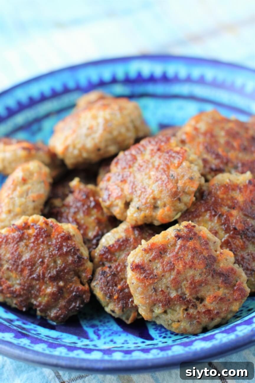 A blue plate filled with golden-brown, freshly fried homemade sausage patties, garnished with fresh herbs.