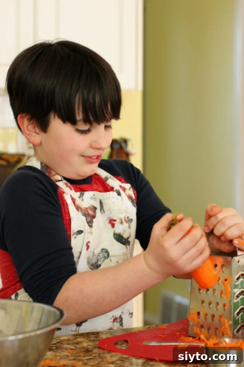 A child, William, diligently grating a carrot on a box grater for the homemade sausage patty mixture.