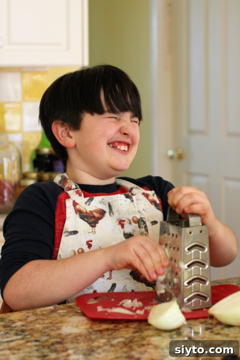 William wincing and closing his eyes while grating an onion for homemade sausage patties, highlighting the tear-jerking effect.