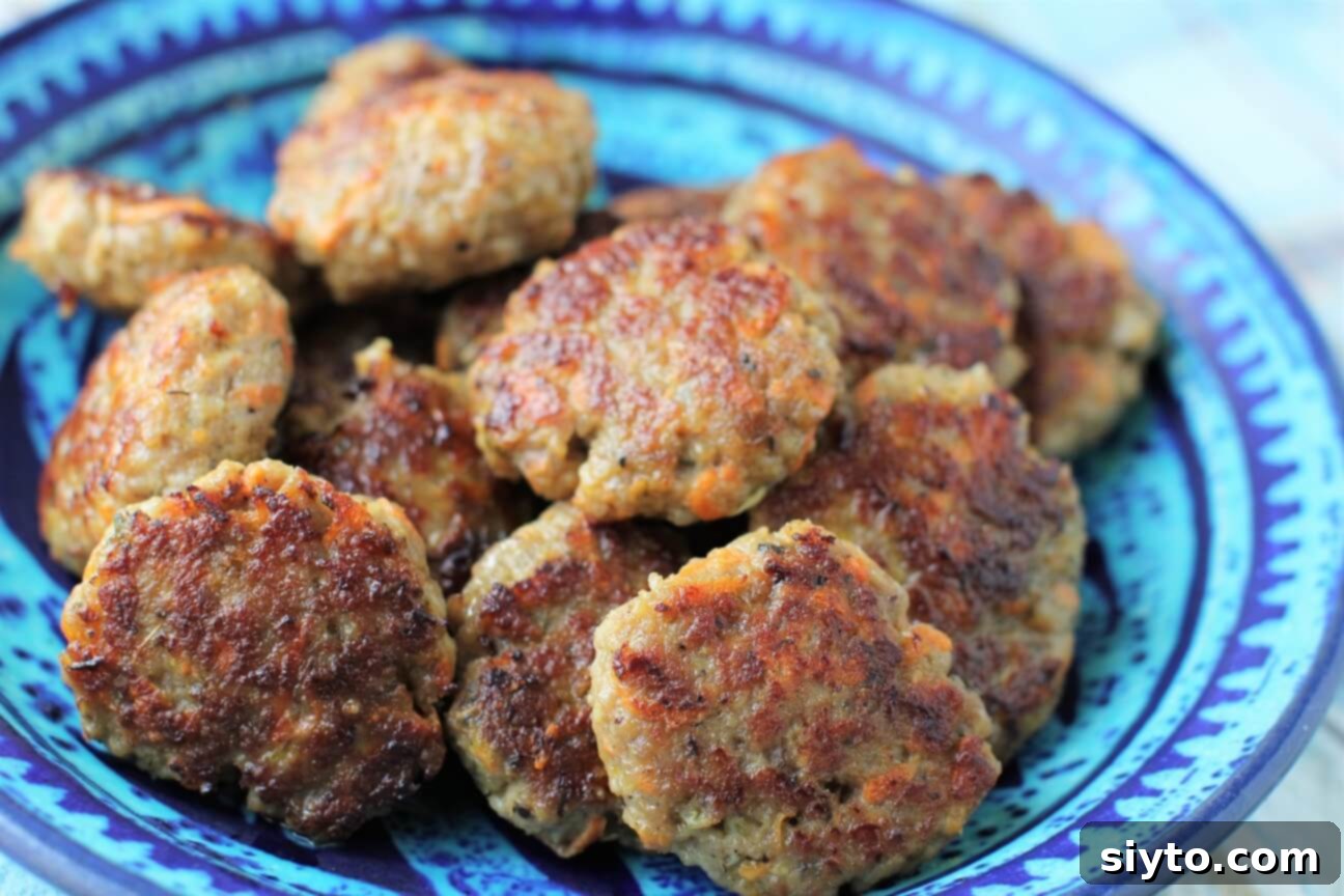 A beautifully plated dish of golden-brown, perfectly fried homemade sausage patties, garnished with fresh rosemary, ready to be enjoyed.