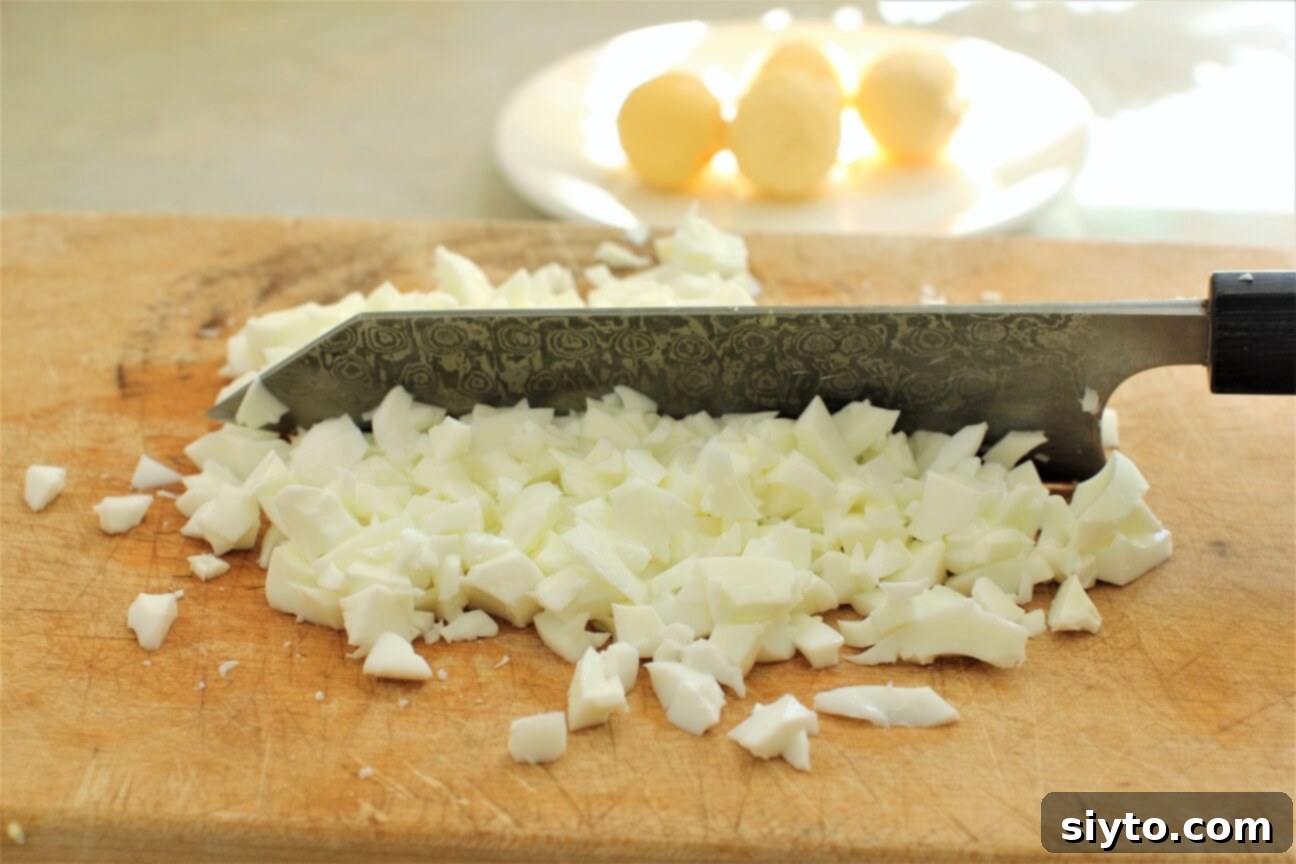 Chopping boiled egg whites on a cutting board, preparing them for the Chive & Egg Pasta Salad.