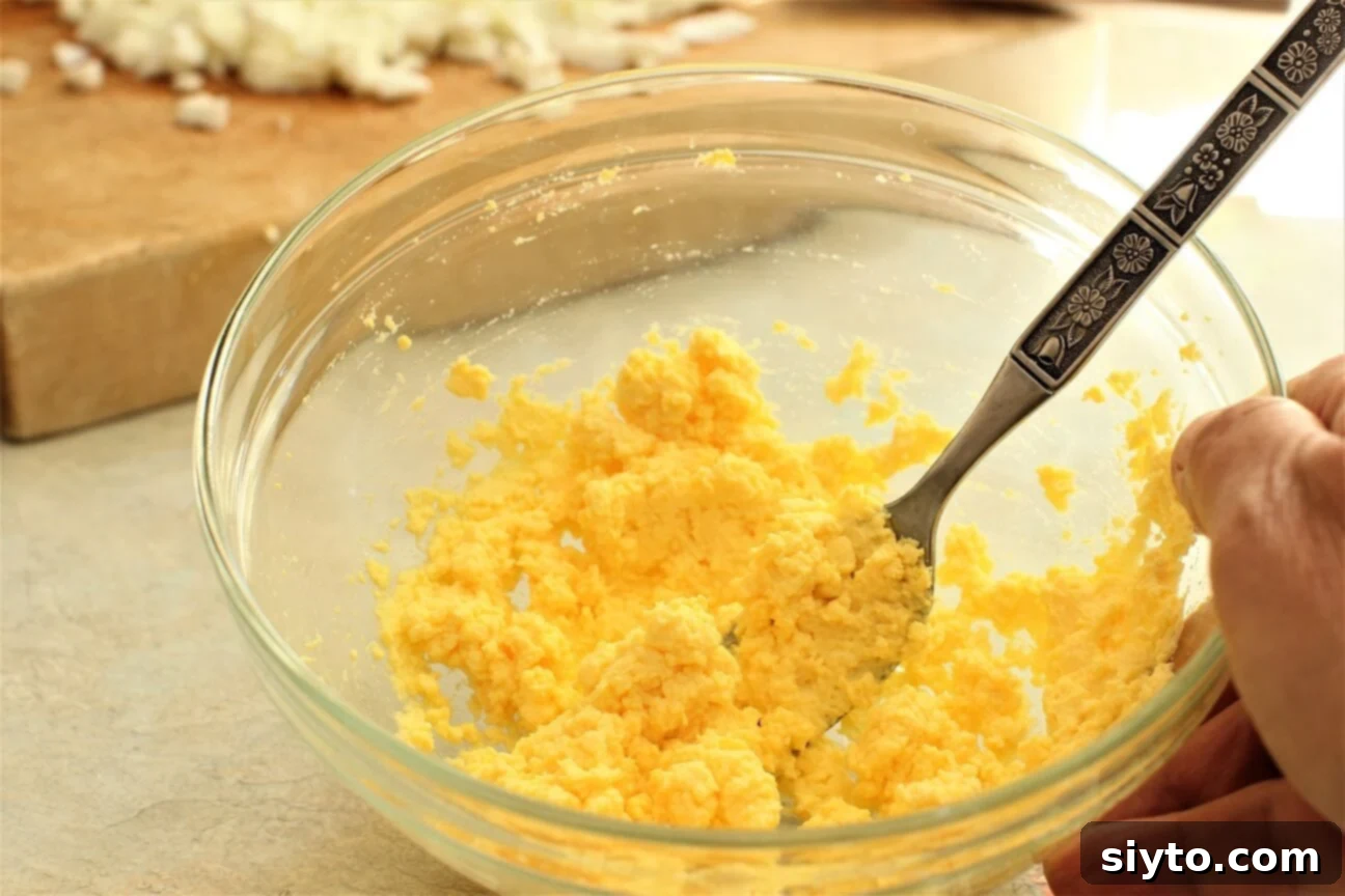 Mashing boiled egg yolks with a fork in a bowl, preparing the base for the creamy dressing.