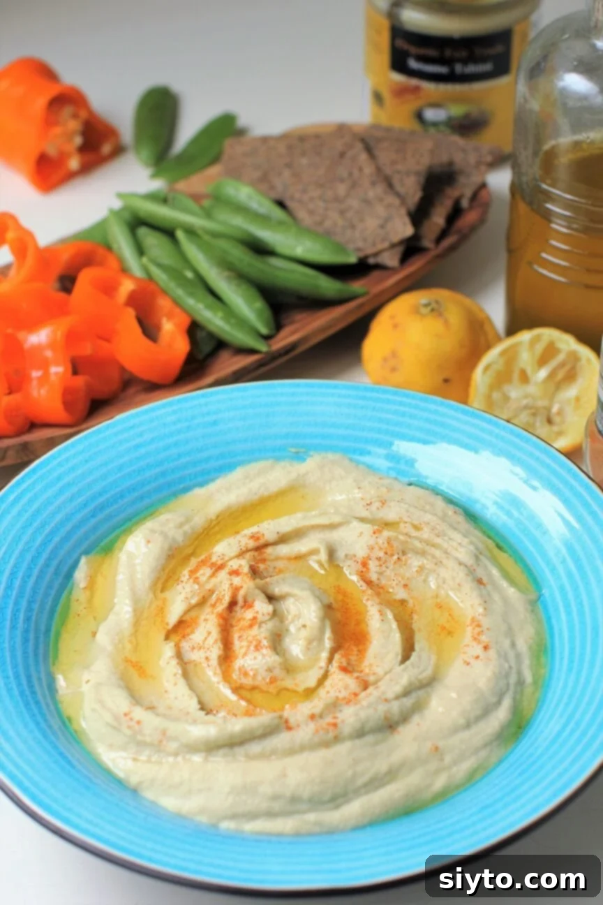 A vibrant blue bowl of homemade hummus served alongside an inviting assortment of crisp fresh vegetables and gourmet crackers, beautifully arranged for a meal or party.