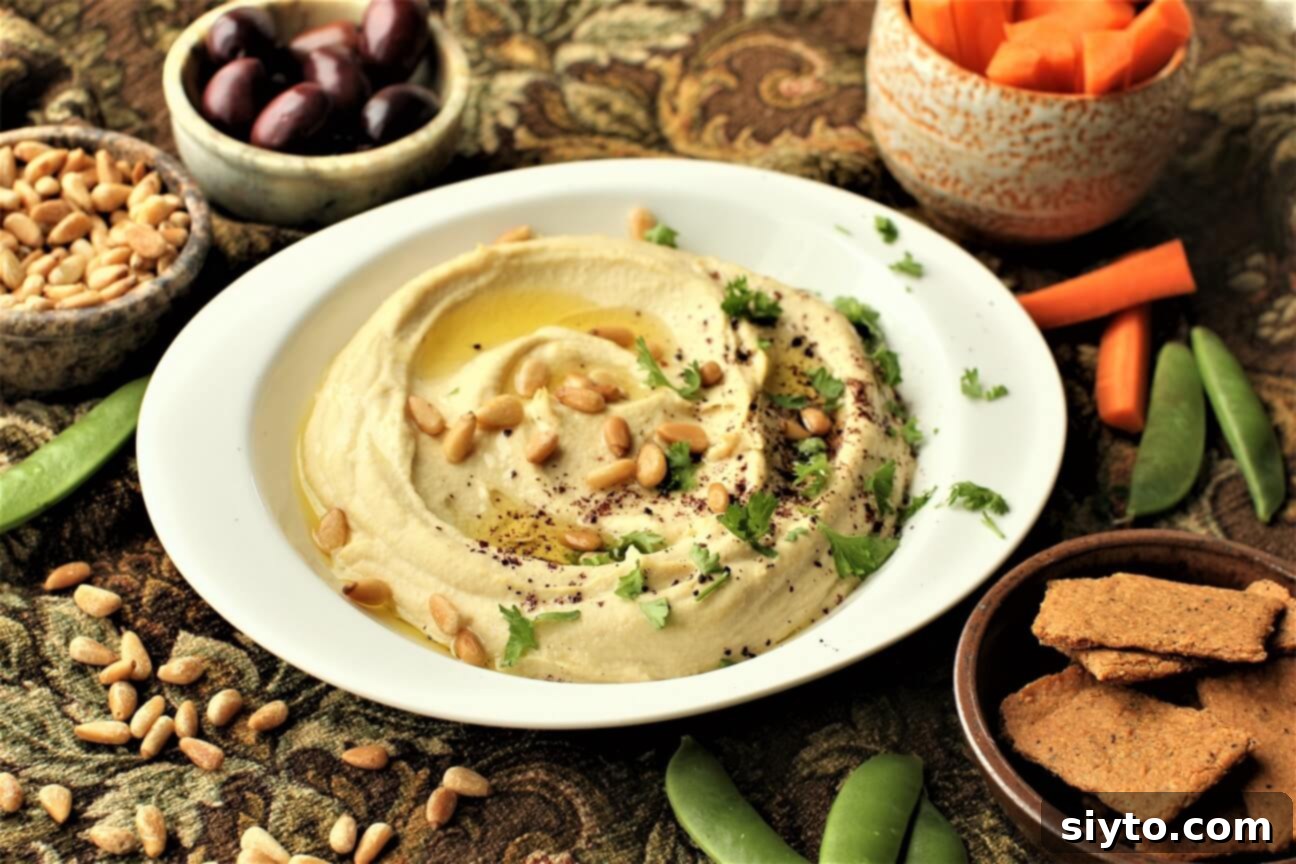 A beautifully presented bowl of creamy homemade hummus, elegantly garnished for a party with olive oil, a dusting of sumac, toasted pine nuts, and fresh parsley sprigs.
