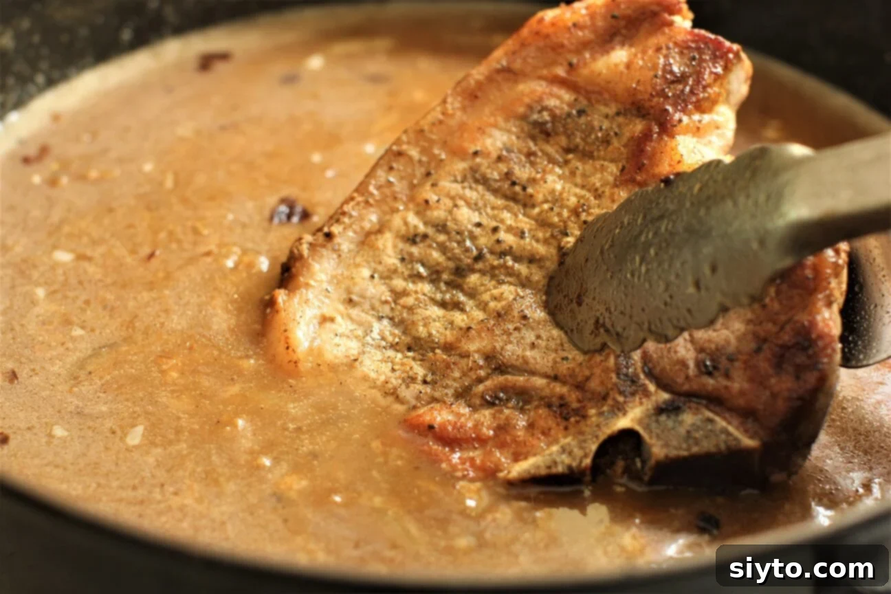Southern Smothered Pork Chops: A Soul Food Classic 7 A pair of tongs gently sliding the first beautifully browned pork chop into the simmering onion gravy, beginning the braising process.