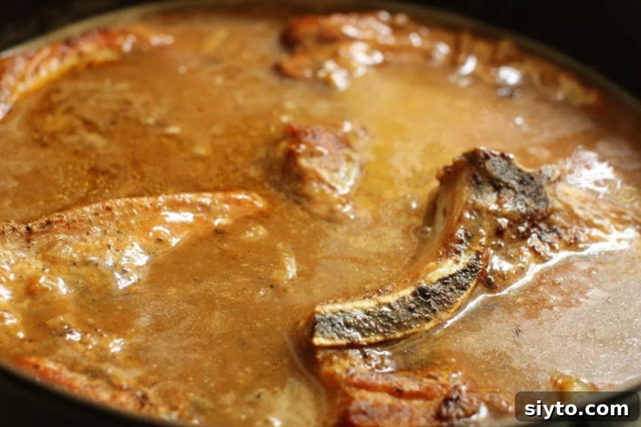 Southern Smothered Pork Chops: A Soul Food Classic 8 All four pork chops fully submerged in the rich, simmering onion gravy, ready for the slow braising process in the oven.
