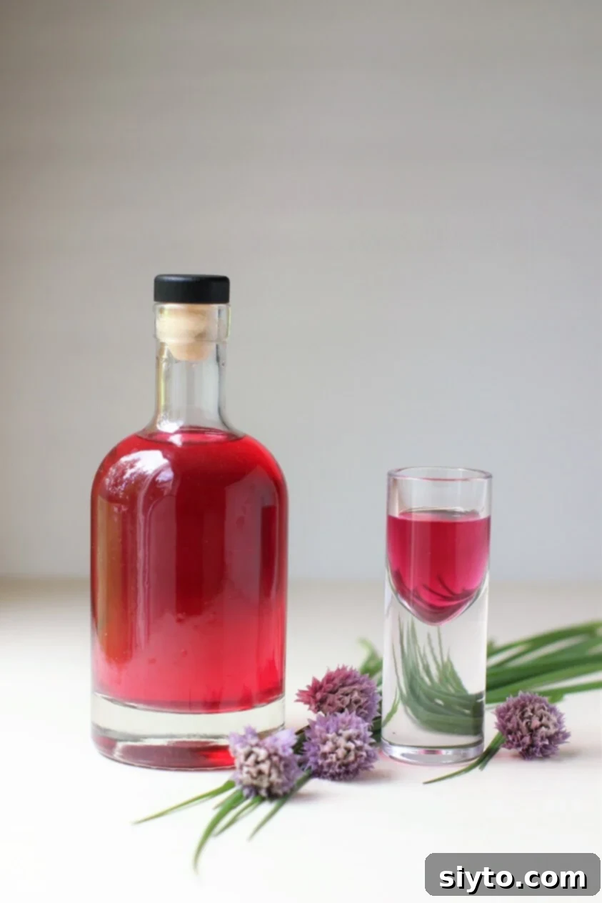 A bottle of homemade chive blossom vinegar with a small shot glass of it beside, showcasing its vibrant pink color