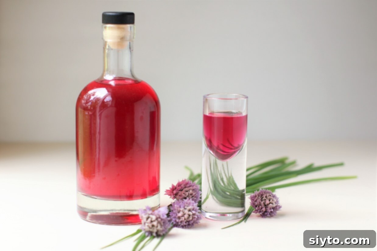 A clear glass bottle filled with beautiful, vibrant pink chive blossom vinegar, standing on a wooden surface