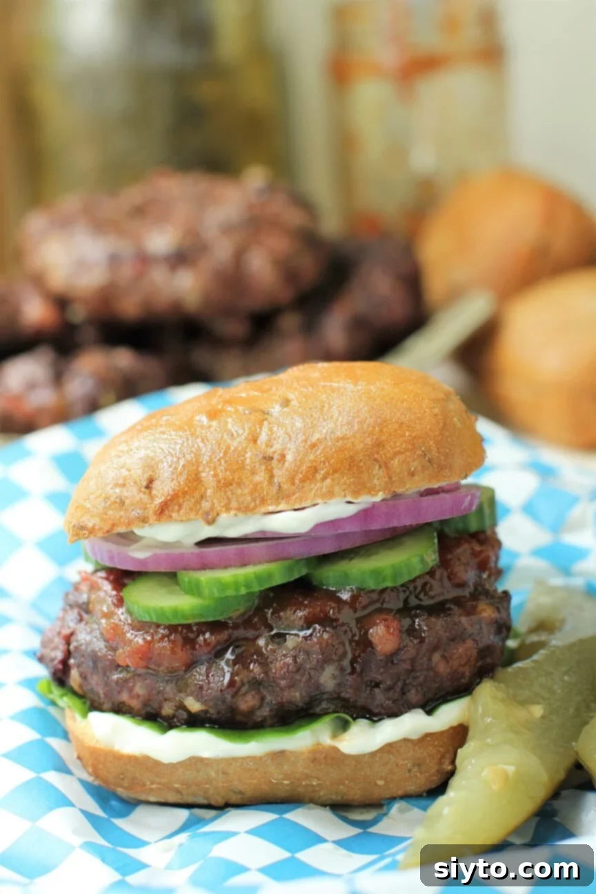 a venison burger on a bun, layered with mayo, lettuce, tomato jam, cucumbers, and red onions