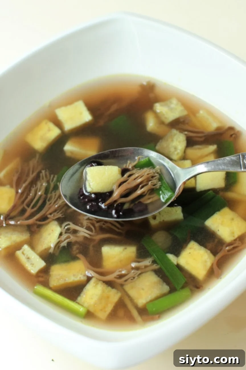 A spoonful of vibrant Asian-style coral mushroom and egg dice soup, showcasing whole coral mushrooms, delicate egg cubes, and dark rice grains in a clear broth.