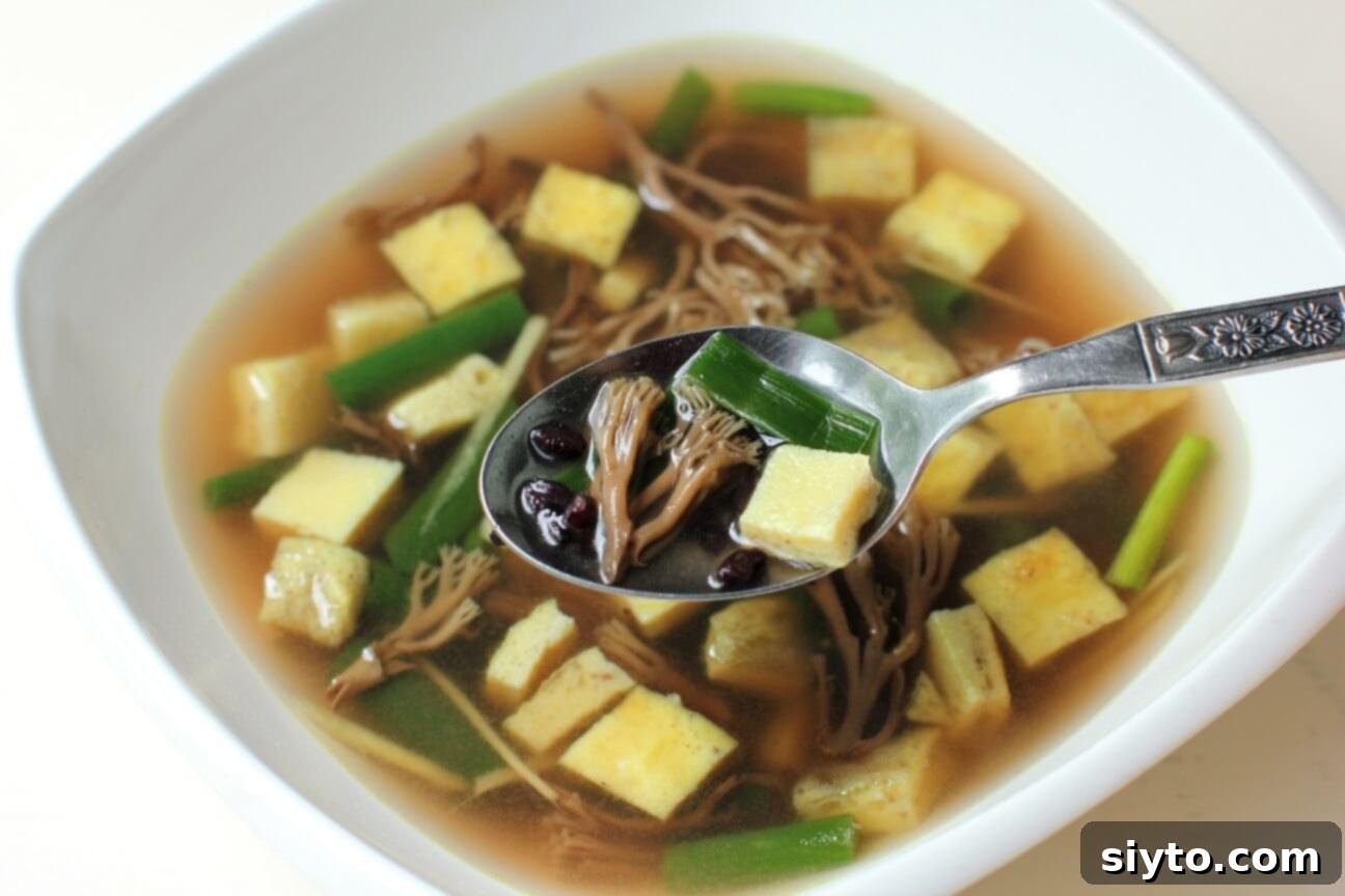 A vibrant bowl of Asian-style coral mushroom and egg dice soup, featuring colorful ingredients and fresh herbs.