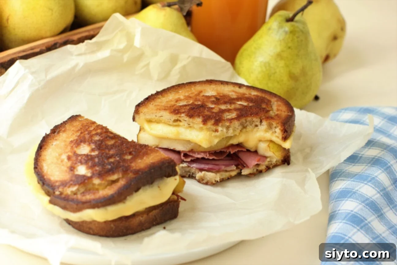 A grilled cheese sandwich with pear and pastrami, cut in half and a bite taken out, showing gooey cheese and fruit