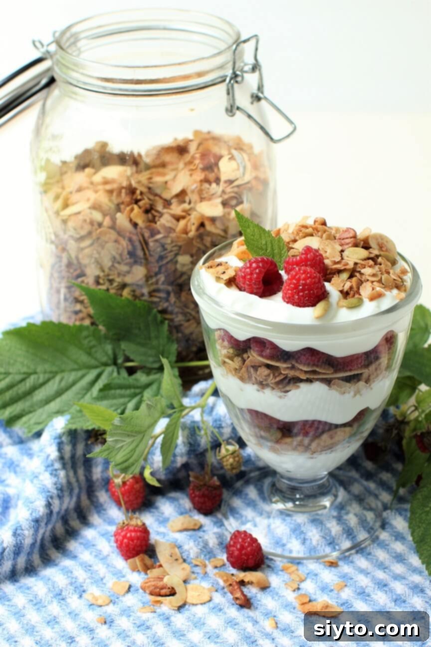 A vibrant breakfast parfait featuring layers of light and crispy granola, creamy yogurt, and fresh, juicy raspberries, presented in a clear glass.
