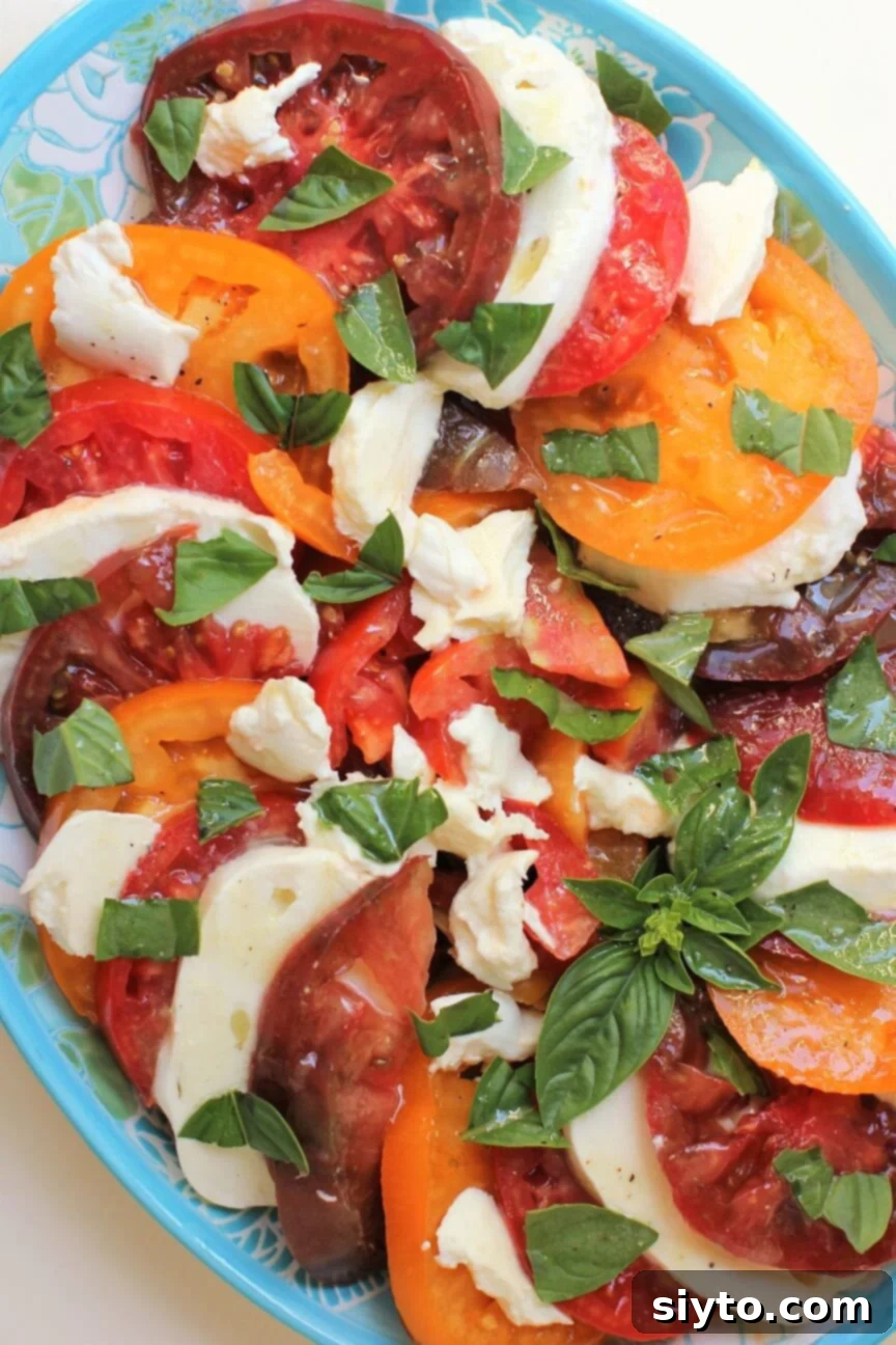 a large platter layered with slices of heirloom tomatoes and fresh mozarella slices, sprinkled with torn basil leaves