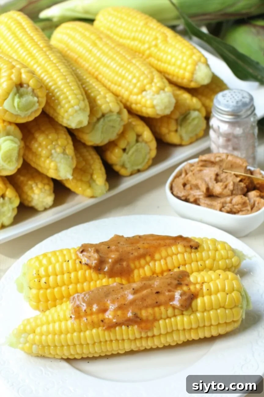 two cobs of corn slathered with chili butter, a stack of cobs in the background