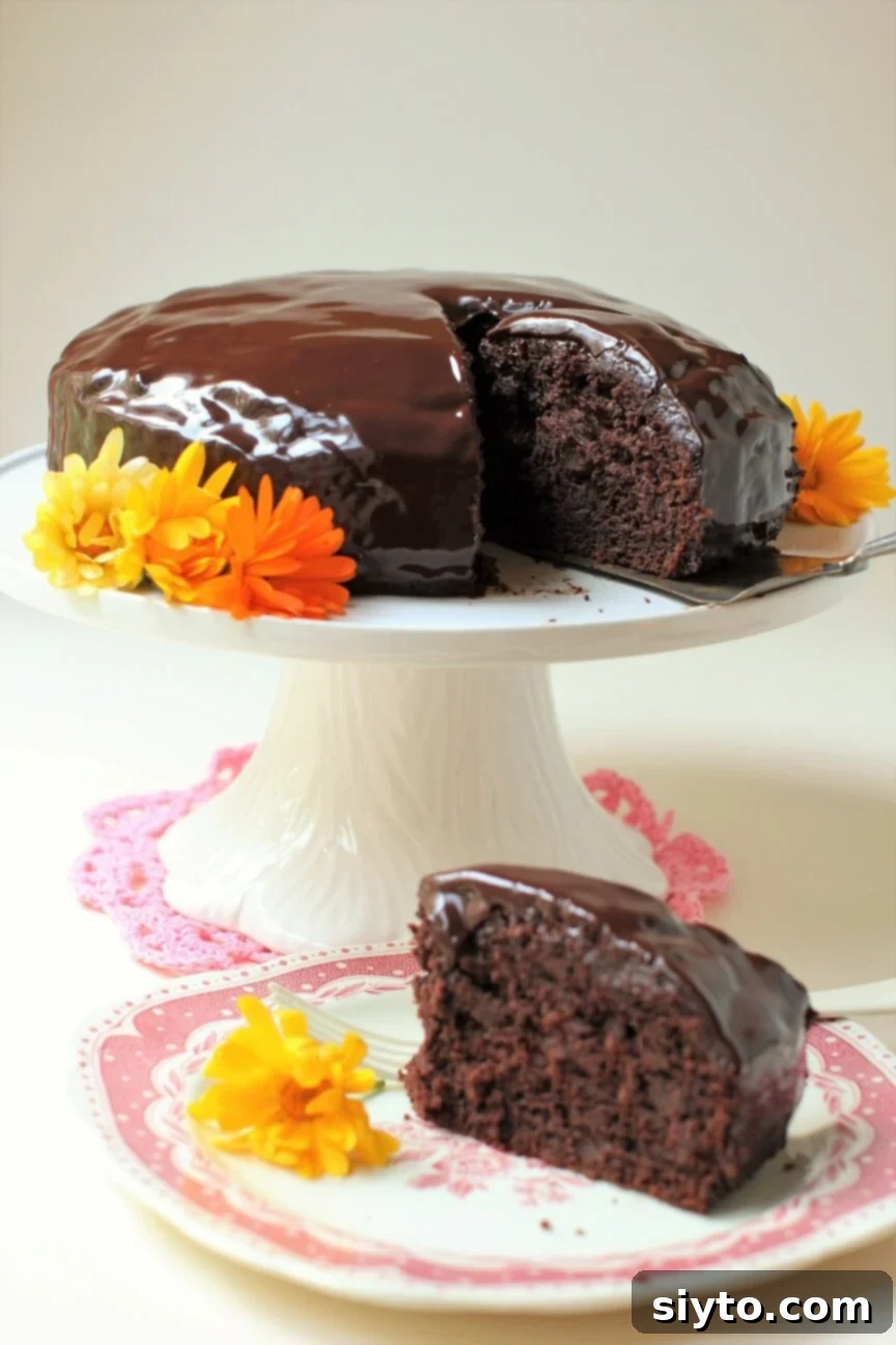 Rich, deeply darkly chocolatey, and almost fudgy Zucchini Chocolate Cake on a pedestal with calendula blossoms, a piece being removed