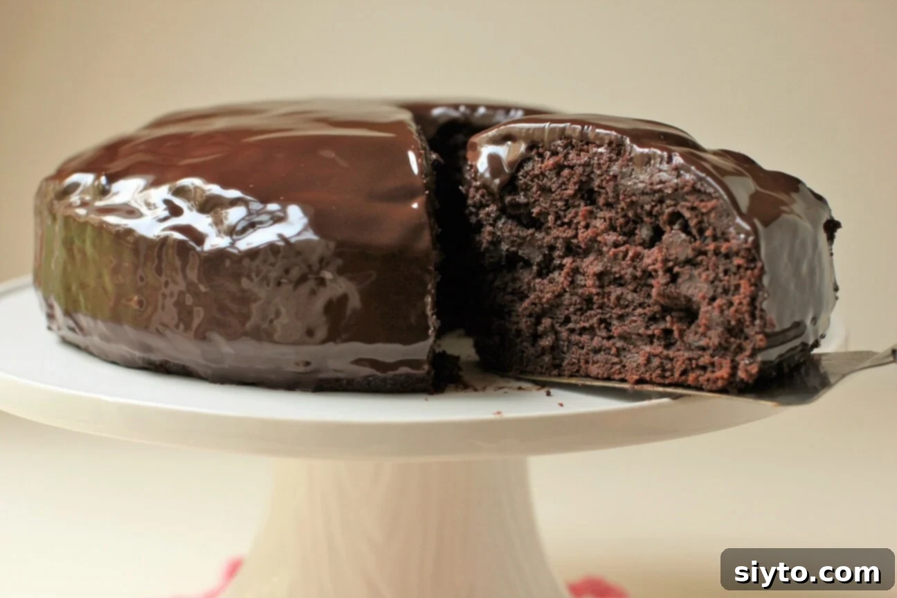 The glorious Zucchini Chocolate Cake sitting atop a pedestal, with one perfect slice in the process of being removed