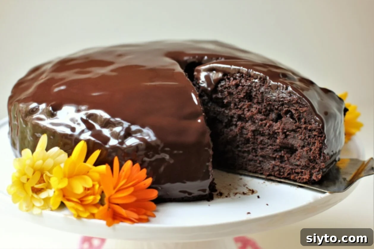 A glorious zucchini chocolate cake presented on a pedestal with calendula flowers, a slice being carefully removed to reveal its moist interior.