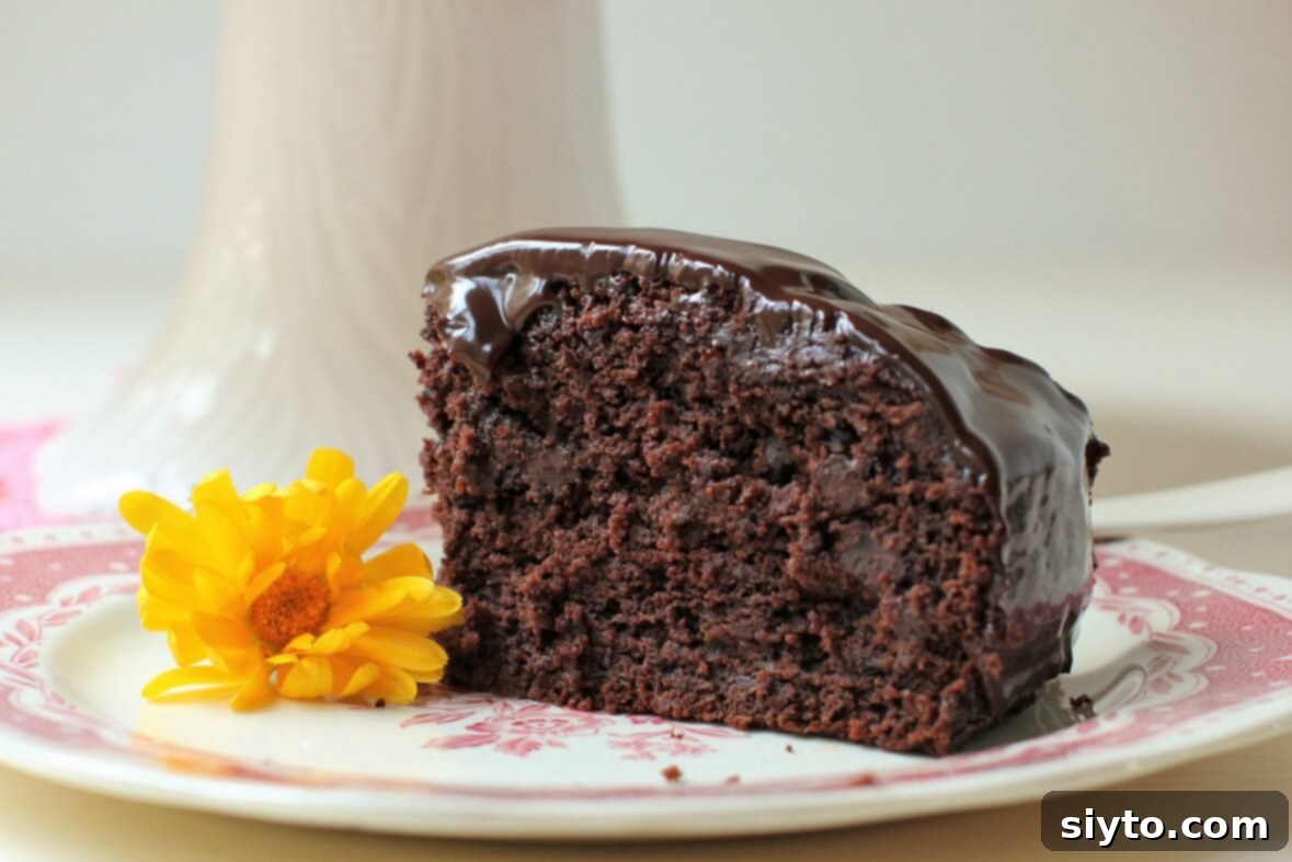 A single, perfectly cut piece of Zucchini Chocolate Cake artfully presented on a white plate, adorned with a delicate calendula blossom