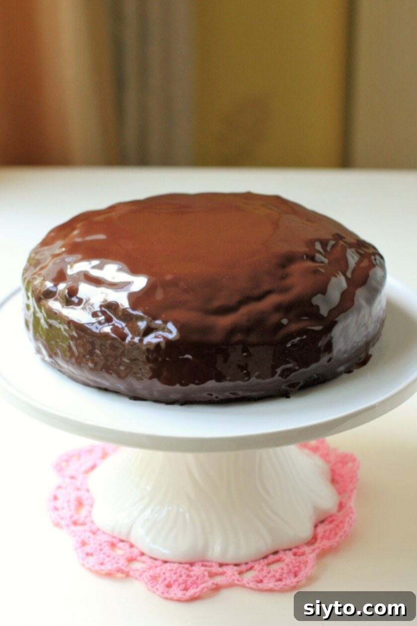 A gorgeously glazed chocolate zucchini cake artfully displayed on a cake stand, glistening under the light
