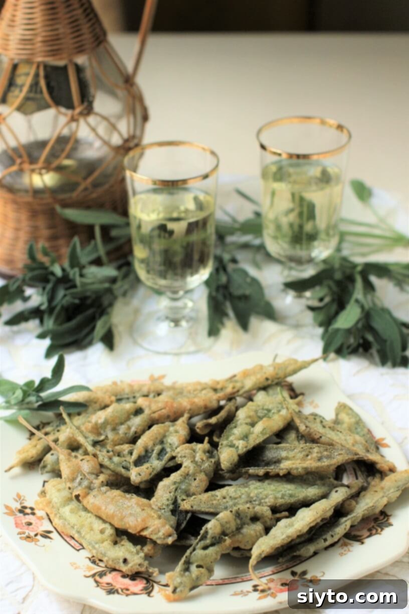 A plate of golden crispy fried sage leaves, with a wine decanter and two glasses in the background, suggesting an elegant appetizer.