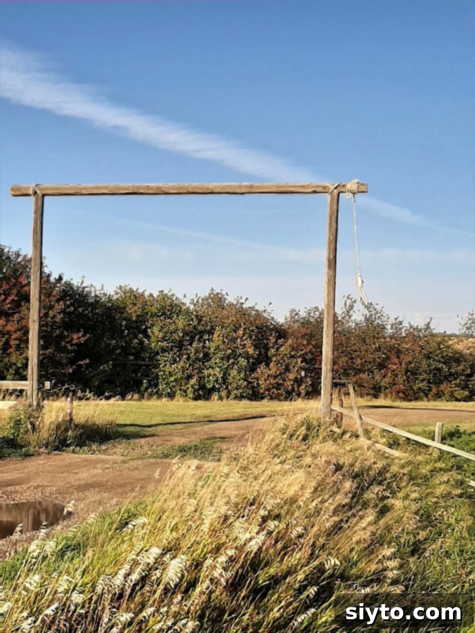 A rustic ranch head gate, weathered by time, adorned with a hangman's noose, standing starkly against a prairie sky.