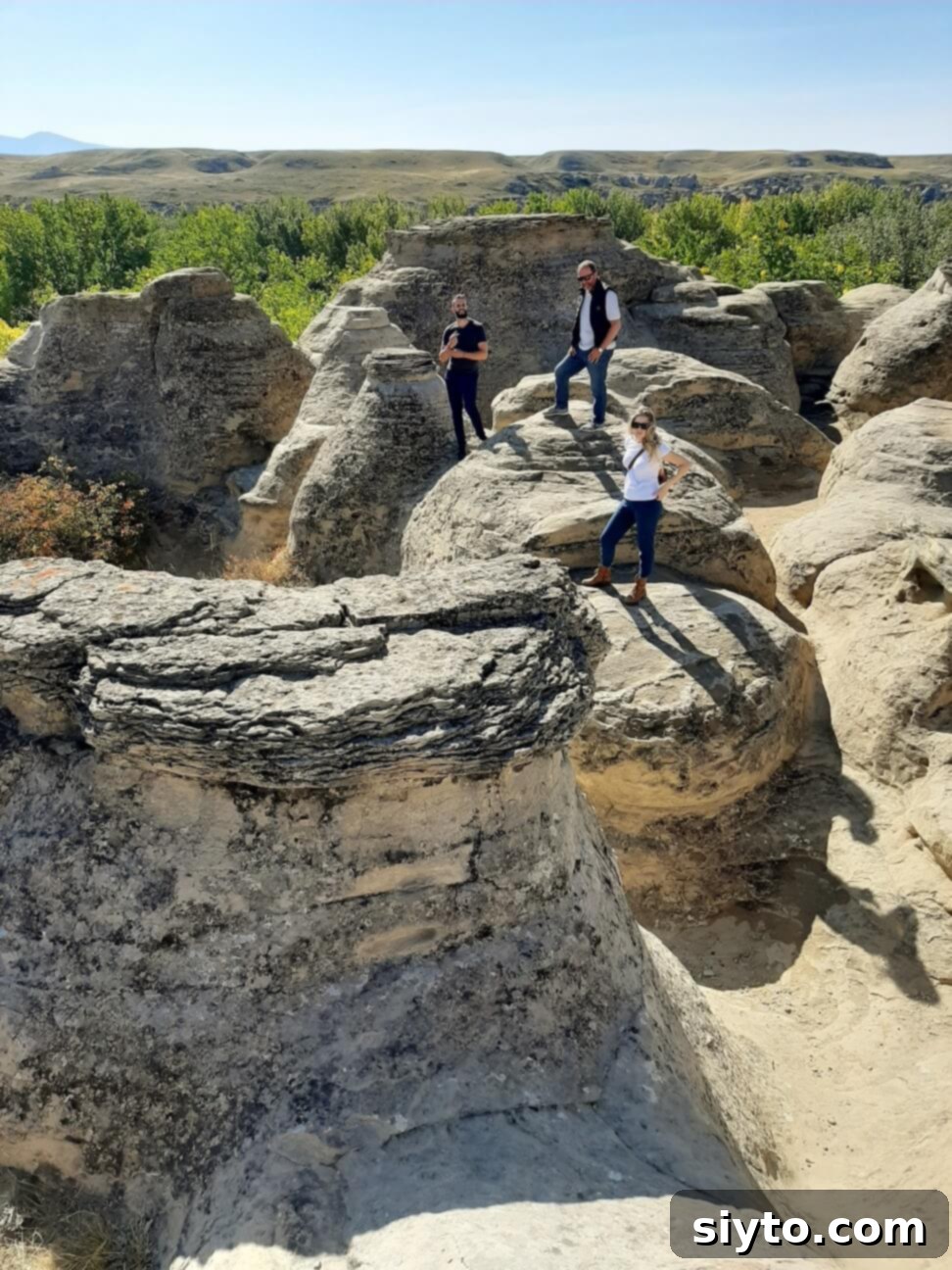 Three people standing triumphantly atop a hoodoo formation in Writing-on-Stone Provincial Park, taking a break from exploring the unique landscape.
