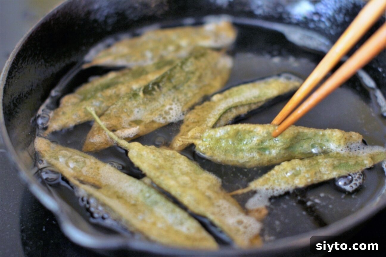 Fresh sage leaves sizzling and turning golden in hot beef tallow in a cast iron skillet, mid-frying process.