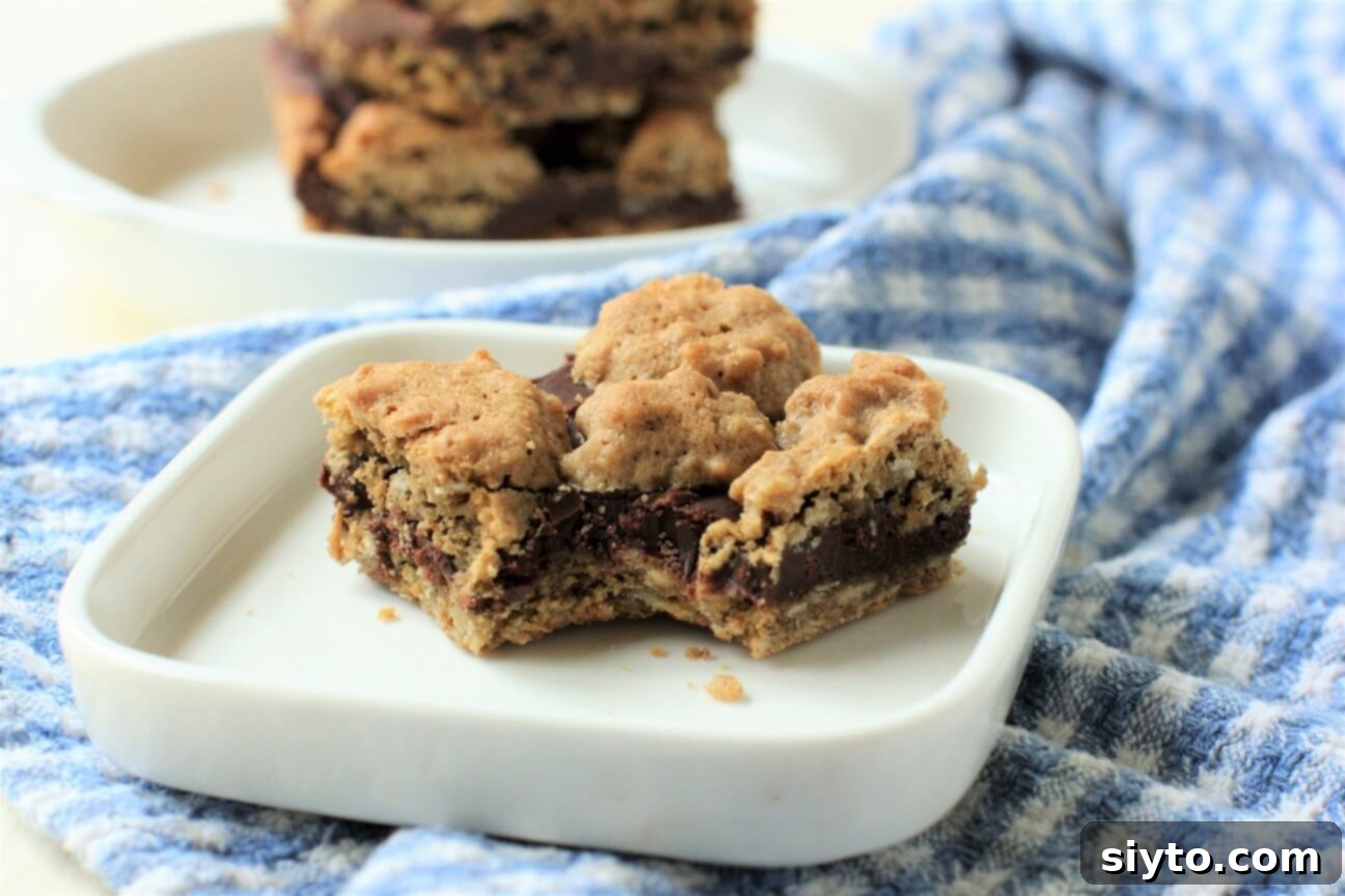 An oat fudge bar with a bite taken out, resting on a blue plate, with a stack of bars behind