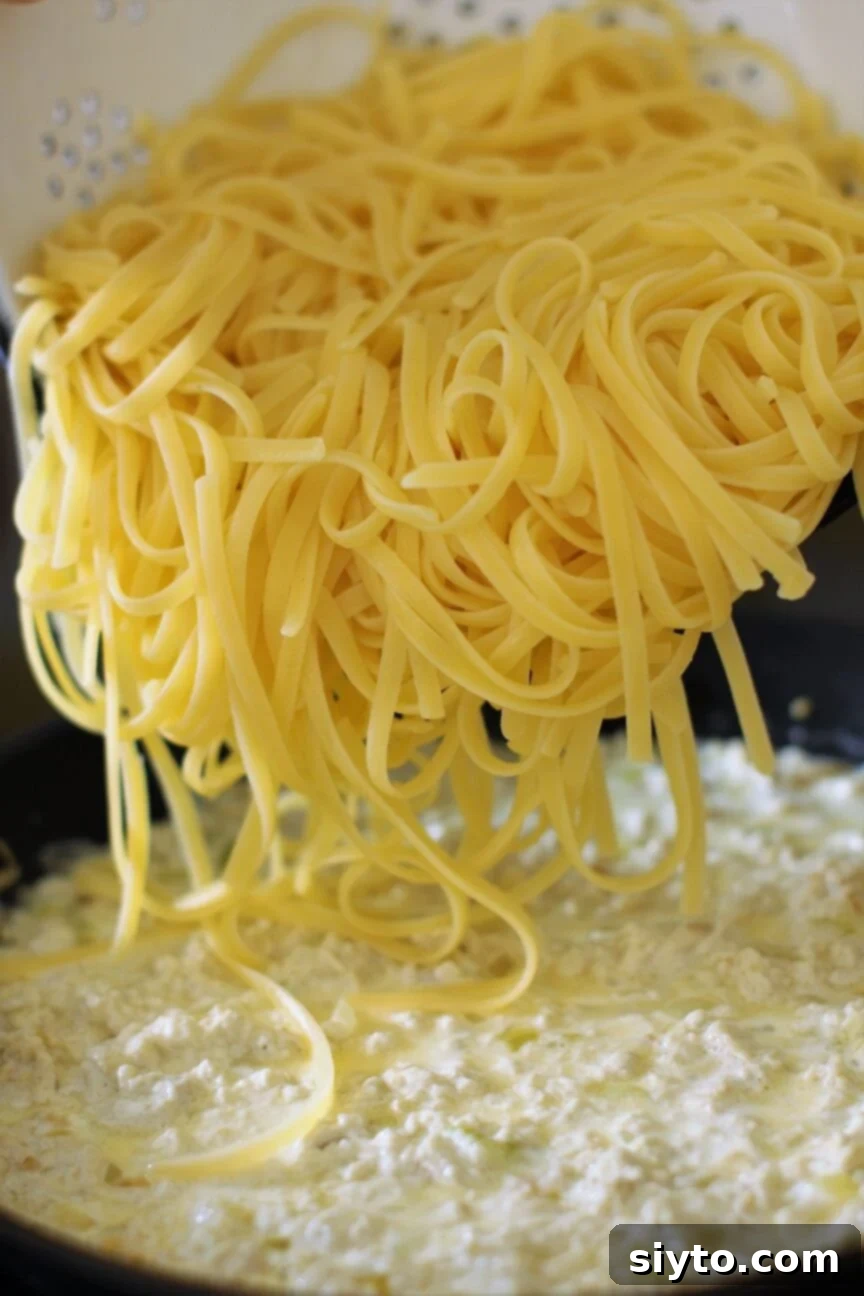 Pouring freshly cooked fettuccine pasta into a skillet with creamy puffball mushroom sauce