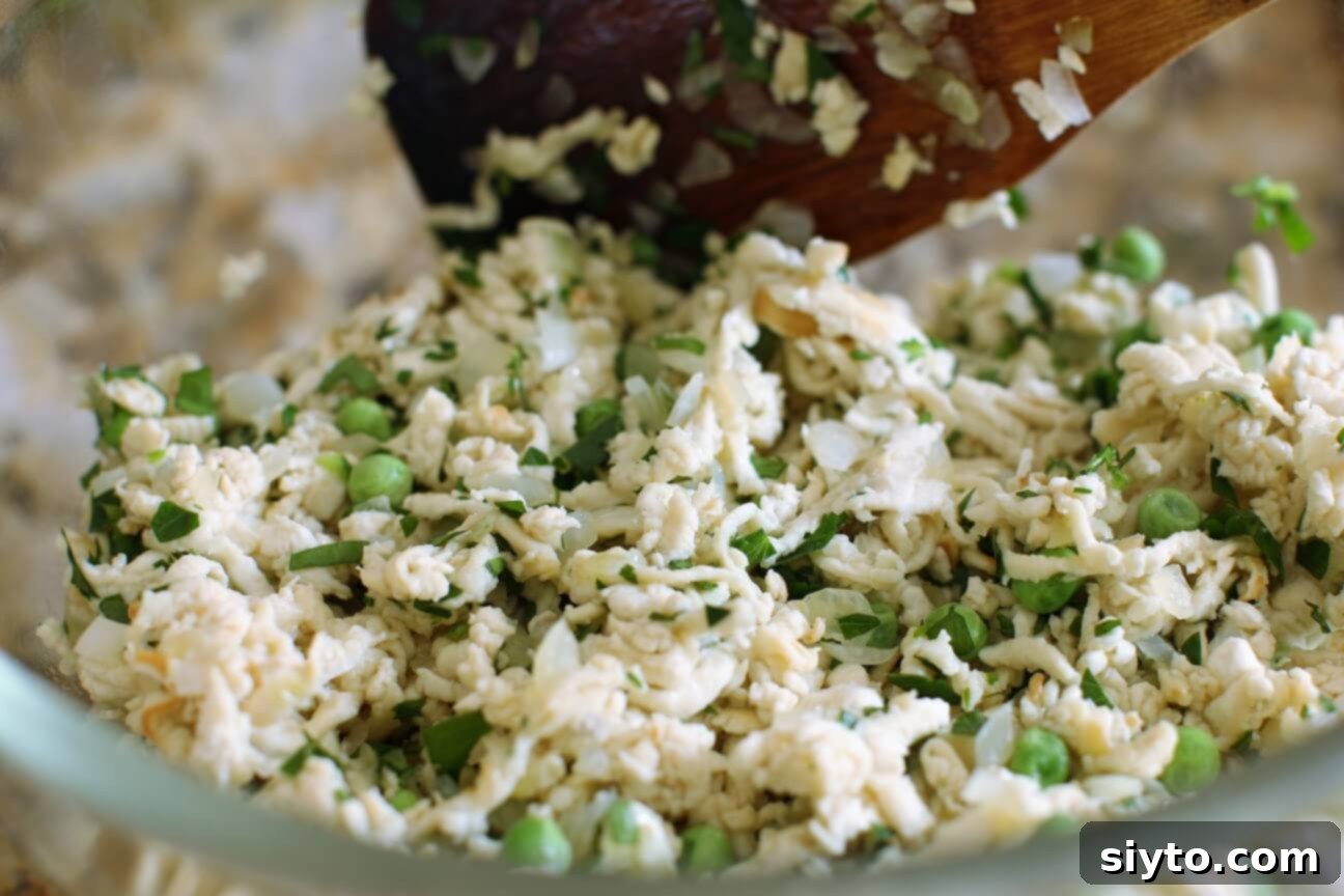 A mixing bowl containing shredded puffball, frozen peas, and fresh herbs, ready to be combined into a patty mixture.