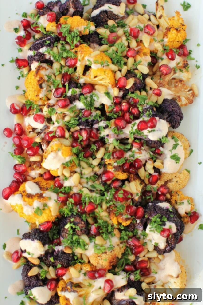 Top-down view of smoky roasted cauliflower, beautifully decorated with ruby-red pomegranate jewels, golden pine nuts, and green parsley flecks.