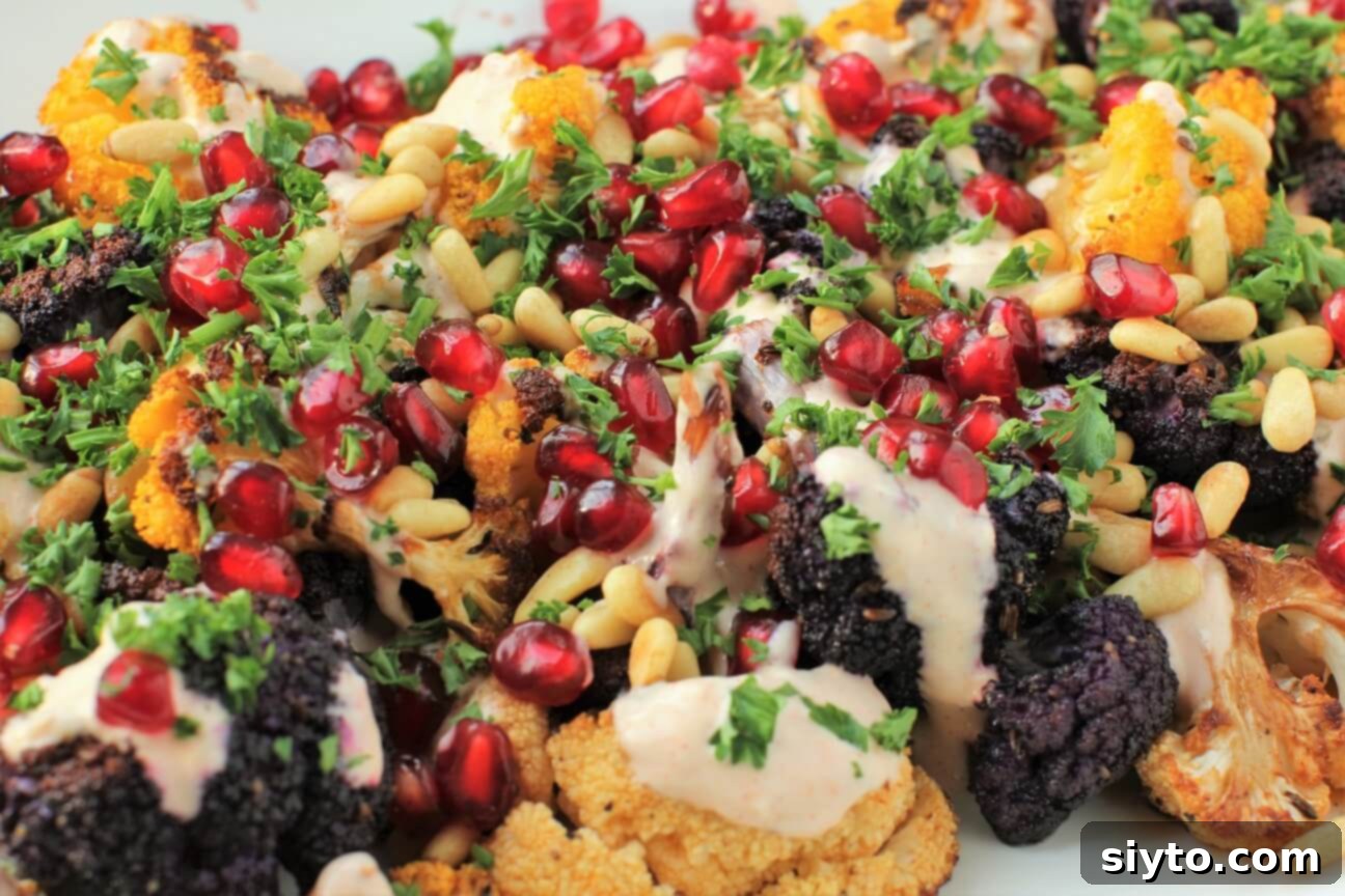 Detailed close-up showing the stunning jeweled toppings, including pomegranate seeds, pine nuts, and parsley, artfully strewn over the roasted cauliflower florets.