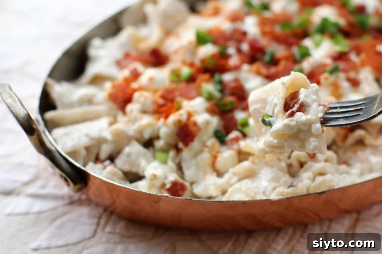 A fork holding a generous bite of Túrós Csusza, covered in creamy sauce and bacon, poised to be eaten.