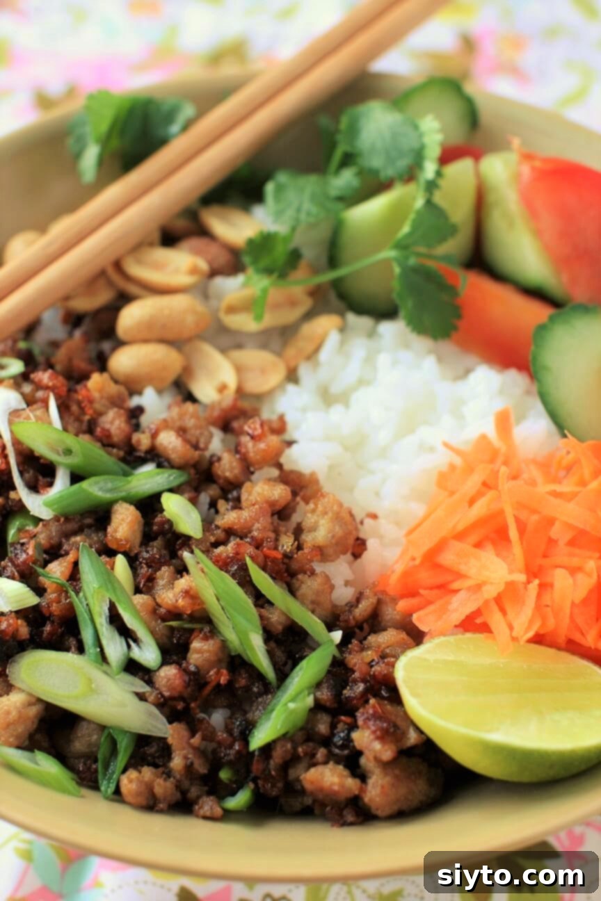 Vietnamese Caramelized Pork Rice Bowl with Chopsticks, featuring sweet, spicy ground pork, fresh herbs, and a lime wedge