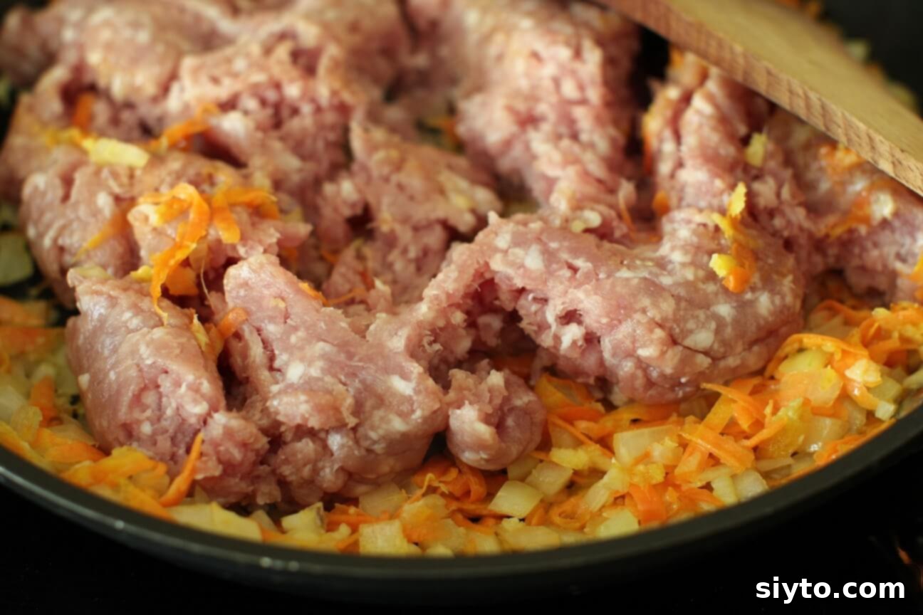 Adding ground pork to the sauteed onions and carrots in a skillet, ready to be browned