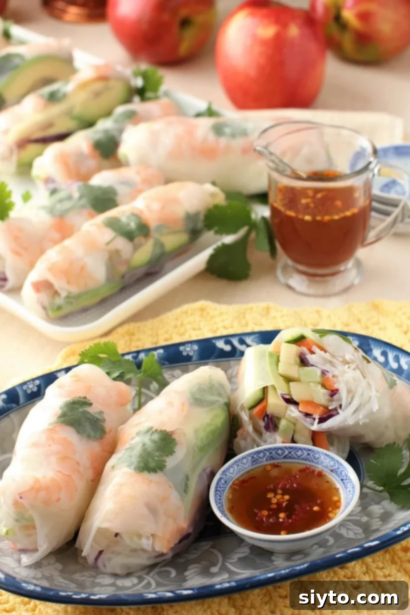 Two vibrant apple and shrimp summer rolls served on a white plate with a dipping sauce bowl beside them, showcasing fresh ingredients.
