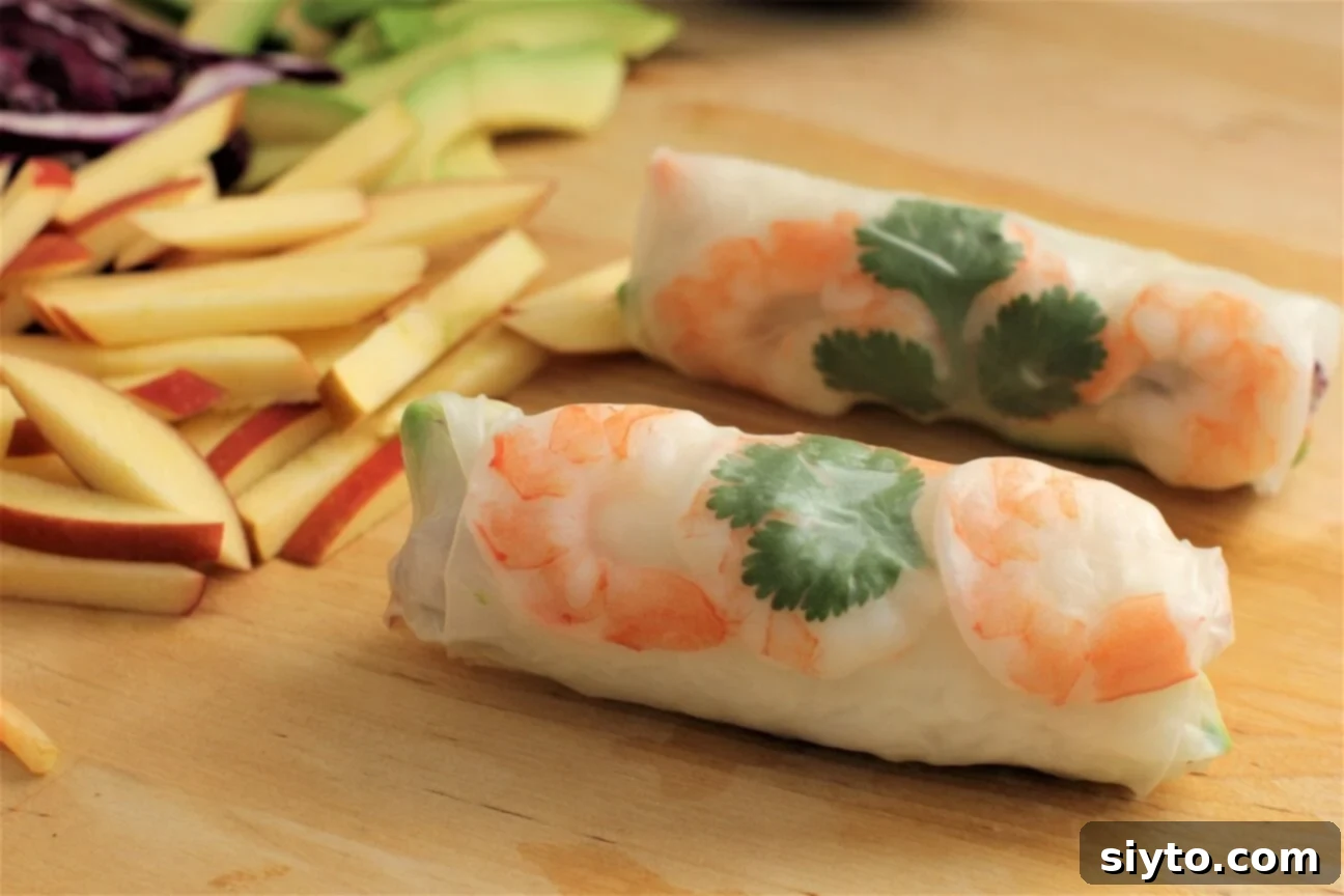 A close-up view of two perfectly rolled summer rolls, showcasing the vibrant pink shrimp and green cilantro leaves visible through the translucent rice paper.