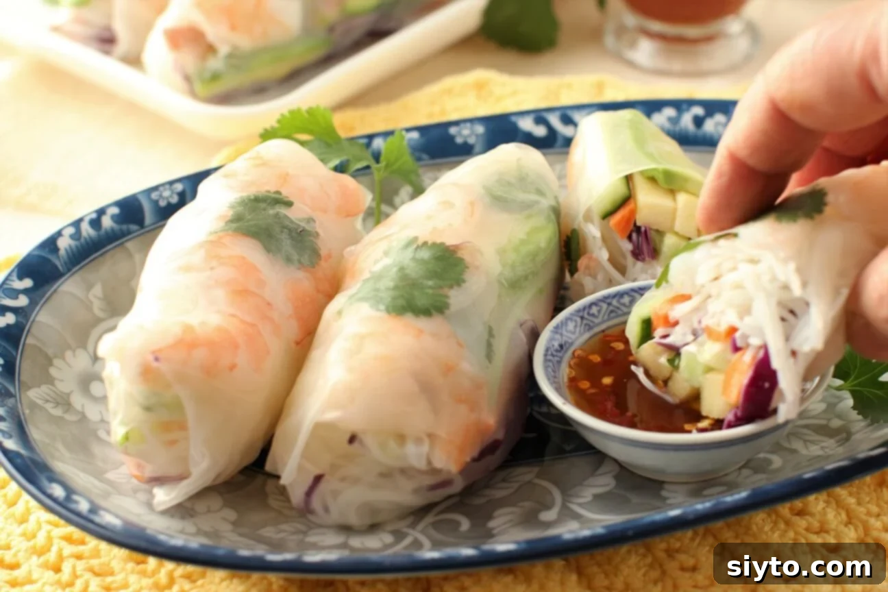 A person gently dips a freshly made apple and shrimp summer roll into a small bowl of savory dipping sauce, highlighting the enjoyment of the meal.