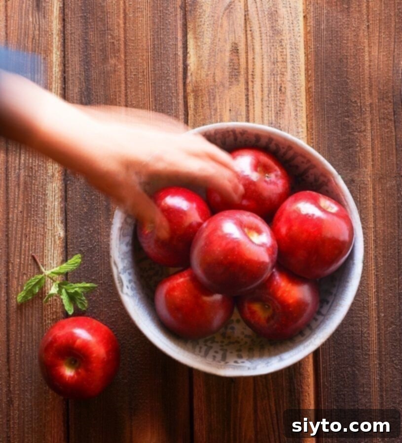 A hand reaching for a vibrant red Cosmic Crisp apple on a rustic wooden surface, highlighting its freshness and appeal.