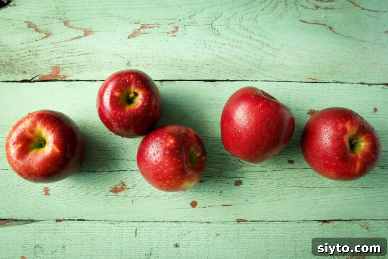 A cluster of radiant red Cosmic Crisp apples neatly arranged on a rustic blue wooden board, emphasizing their fresh and pristine quality.