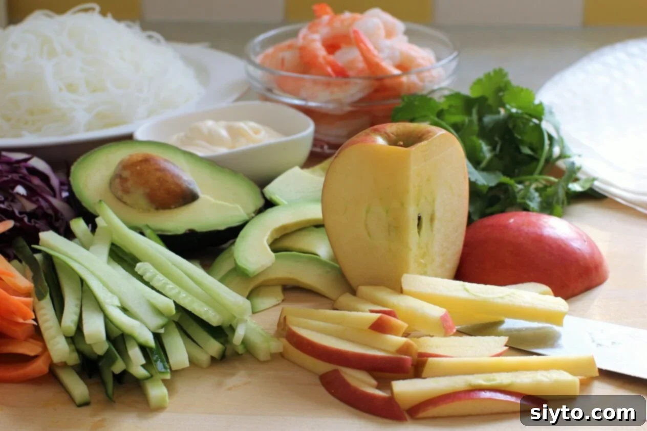 A meticulously arranged spread of fresh ingredients for summer rolls, including cooked shrimp, sliced Cosmic Crisp apples, various vegetables, and rice vermicelli, ready for assembly.