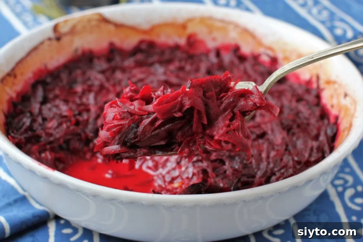 A spoon lifting a generous serving of luscious red beet gratin from a baking dish, highlighting its creamy texture and vibrant color.