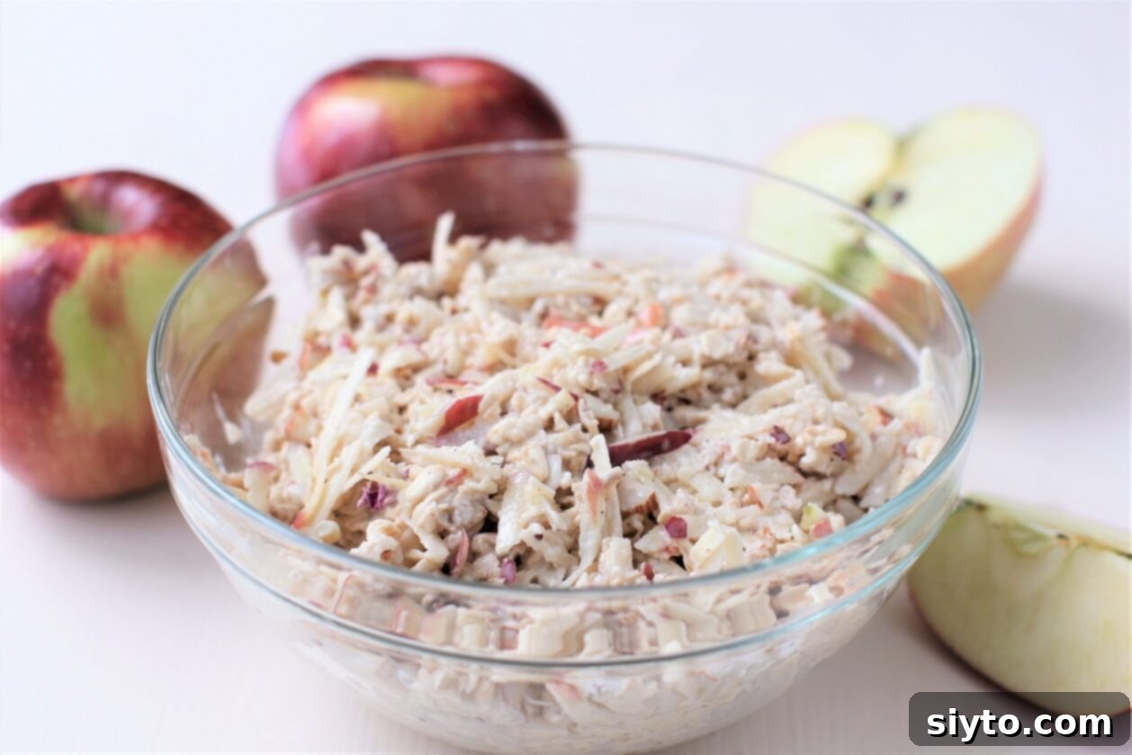 clear glass bowl of muesli, with apples behind