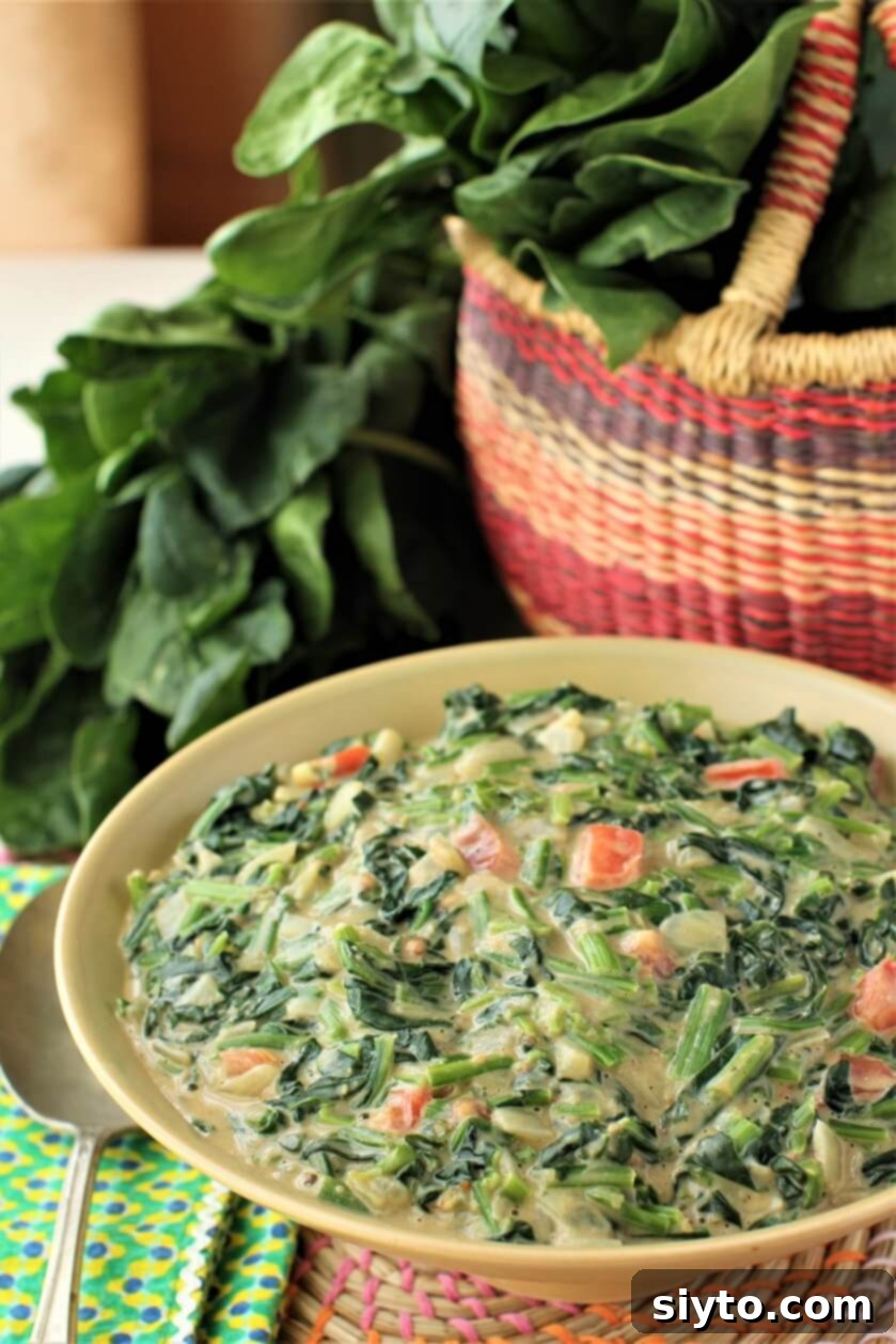 bowl of peanut butter creamed spinach with basket of spinach behind, showcasing creamy texture