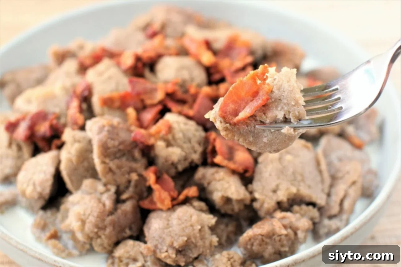 A single plump Stäerzelen buckwheat dumpling on a fork, garnished with a piece of crispy bacon, highlighting its inviting texture.