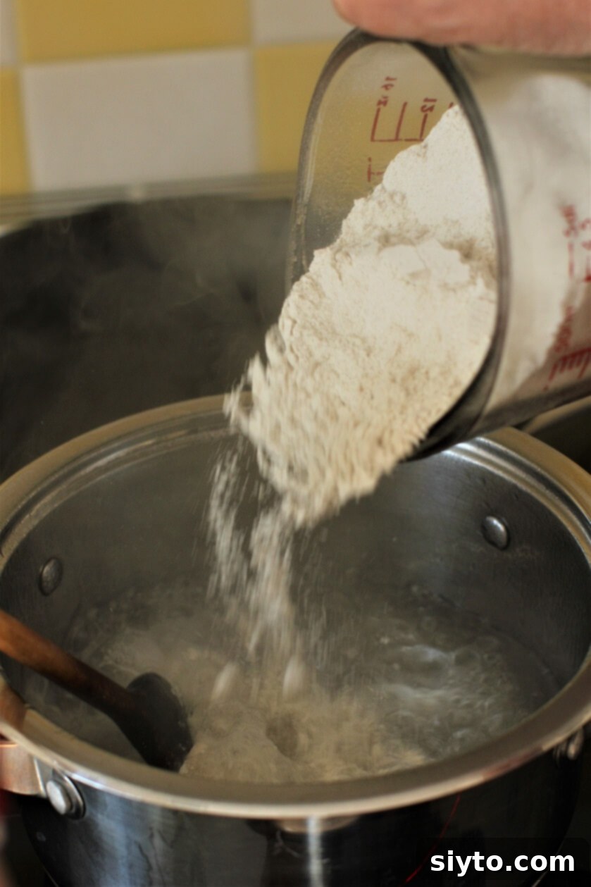 Pouring buckwheat flour in a continuous stream into boiling water while stirring vigorously, demonstrating the initial step of dough preparation for Stäerzelen.