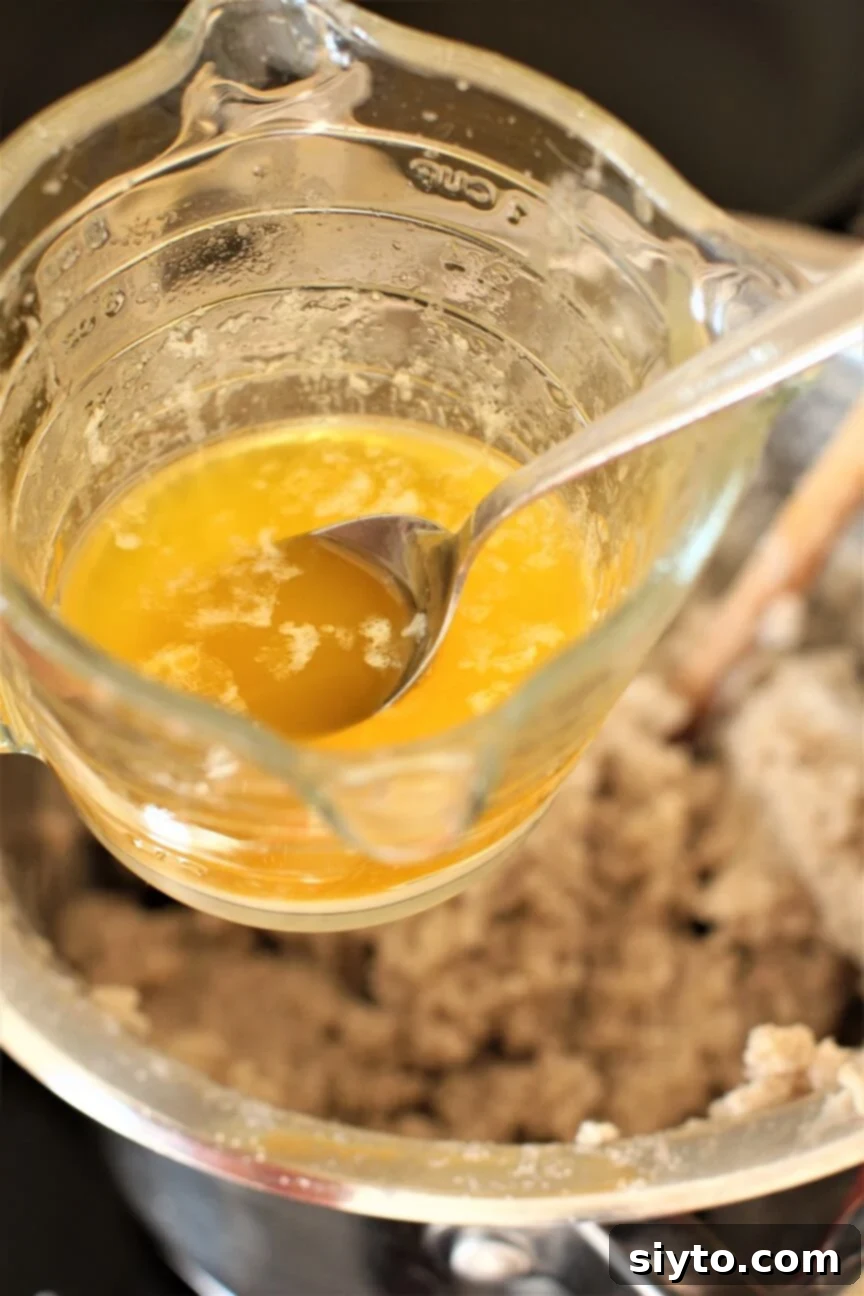 A spoon being dipped into a bowl of melted butter, preparing it for scooping and shaping the buckwheat dumpling dough.