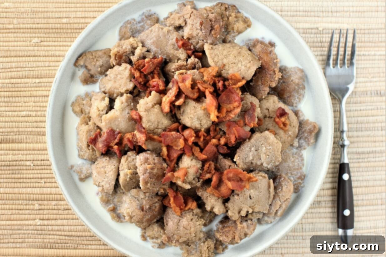 A top-down view of a plate abundantly filled with Stäerzelen buckwheat dumplings, served with crispy bacon bits and a warm milk sauce, inviting a comforting meal.